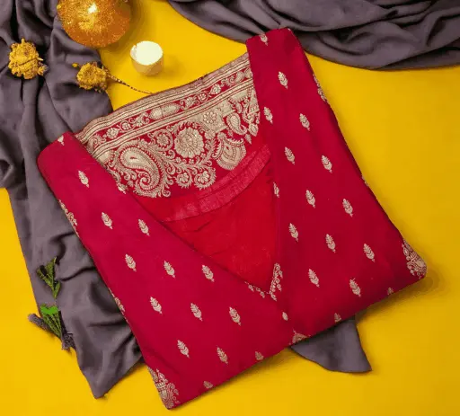Elegant red Banarasi silk sleeveless lining Kurta featuring a rich golden paisley zari border on the back yoke and small scattered motifs all over. This custom-stitched bridal kurta is neatly folded and displayed on a bright yellow background with grey draped fabric and golden accessories, representing premium ladies' boutique tailoring services by Tailorboutiques.com.