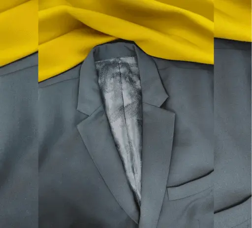 Premium charcoal grey men's coat featuring a sharp notch lapel and luxurious patterned inner lining. This custom-stitched suit jacket is displayed on a yellow fabric background, representing the high-quality gents' tailoring and bespoke coat pant stitching services provided by Tailorboutiques.com.