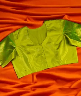 Vibrant Raw Mango green silk saree blouse featuring elbow-length sleeves with self-woven jacquard motifs and a classic V-neckline. This custom-stitched designer blouse is displayed on a contrasting orange background, showcasing the premium ladies' boutique stitching and saree blouse tailoring services offered by Tailorboutiques.com.