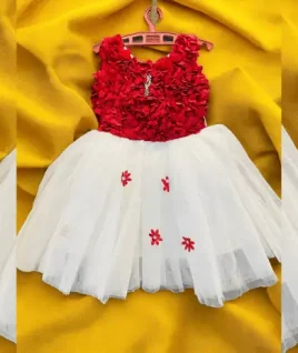 Charming red and white party wear frock for girls, featuring a textured 3D floral bodice and a voluminous white tulle skirt with scattered red flower appliqués. This custom-stitched children's gown is displayed on a hanger against a yellow background, highlighting the expert kids' wear tailoring and designer boutique services offered by Tailorboutiques.com.